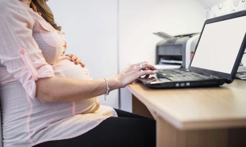 midsection-view-pregnant-woman-using-laptop-wooden-desk-min